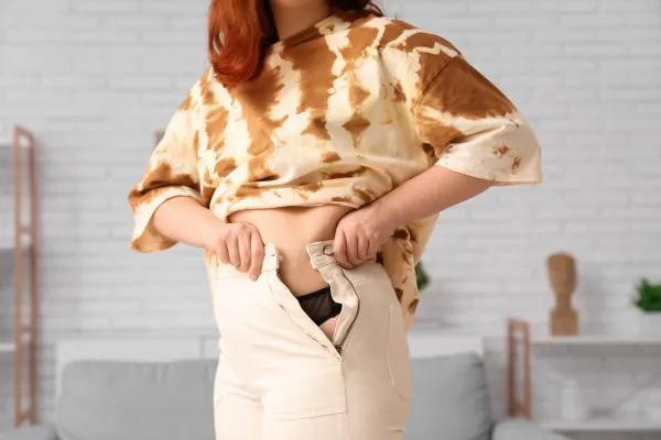 Image of woman trying to do her trousers up after pregnancy weight gain Abbotsbury